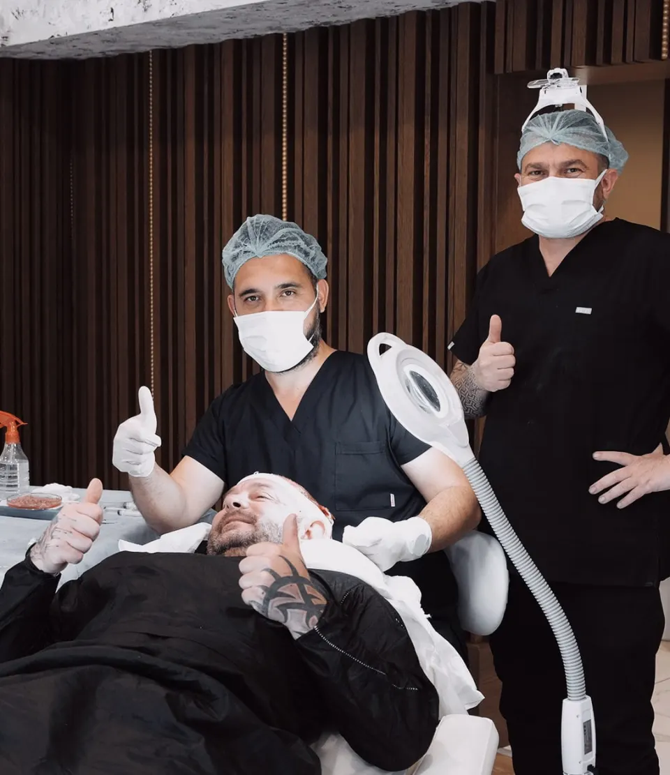 Two clinicians in scrubs, masks and surgical caps beside a patient during a procedure.